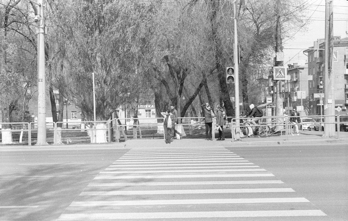 Pedestrians and a cyclist waiting at a marked crosswalk at a city intersection